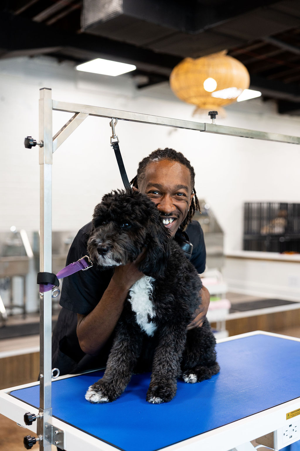 FreshCoat Grooming Lead Groomer smiling with a freshly groomed black and white ShiPoo on a professional grooming table in Charlotte, NC